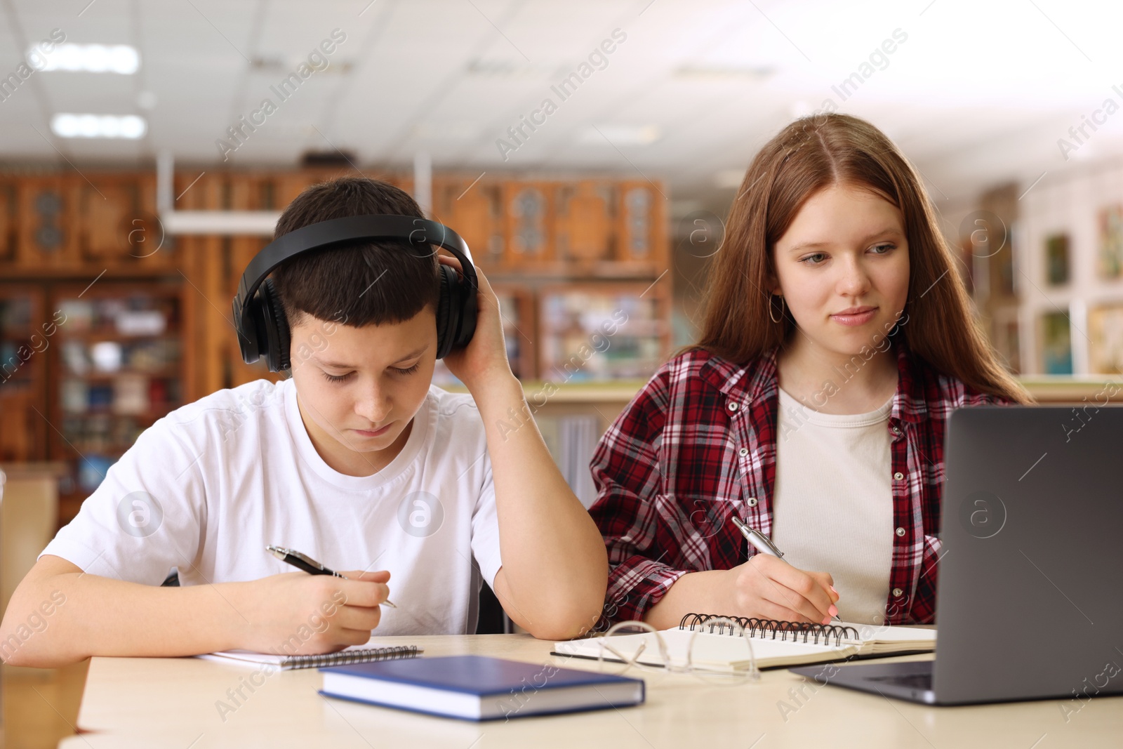 Photo of Teenage friends with laptop doing homework at desk in library