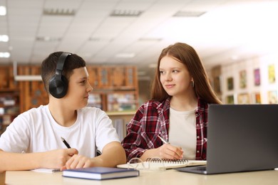 Photo of Teenage friends with laptop doing homework at desk in library