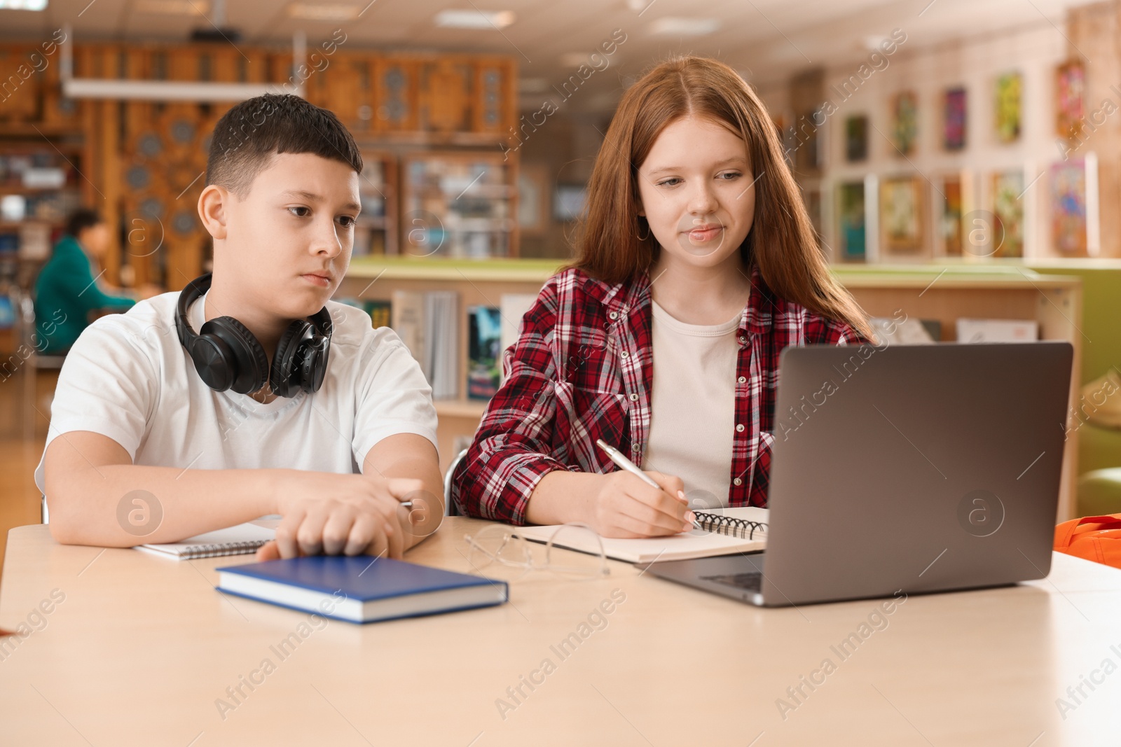 Photo of Teenage friends with laptop doing homework at desk in library