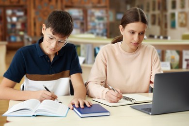 Photo of Teenage friends with laptop doing homework at desk in library