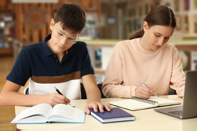 Photo of Teenage friends with laptop doing homework at desk in library