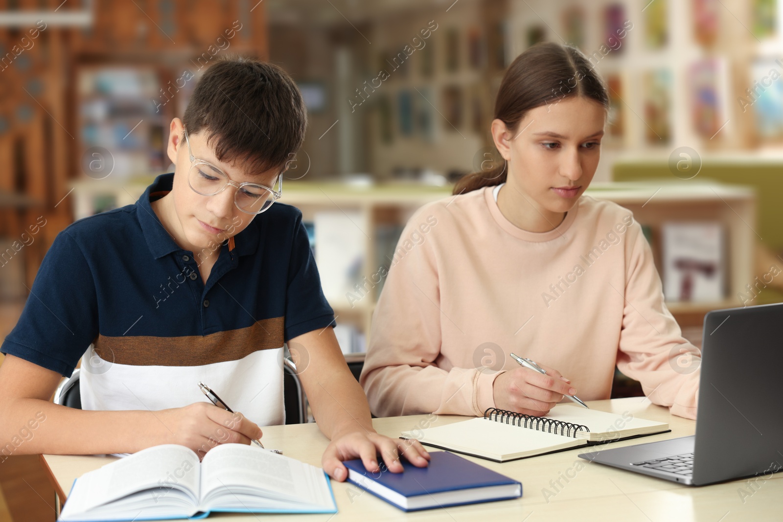 Photo of Teenage friends with laptop doing homework at desk in library