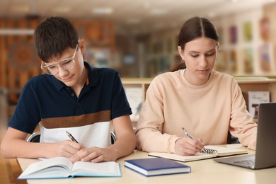 Photo of Teenage friends with laptop doing homework at desk in library