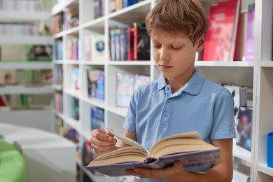 Photo of Teenage boy reading book in public library