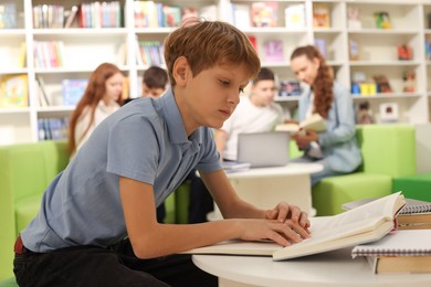 Photo of Teenage boy reading books at table in public library