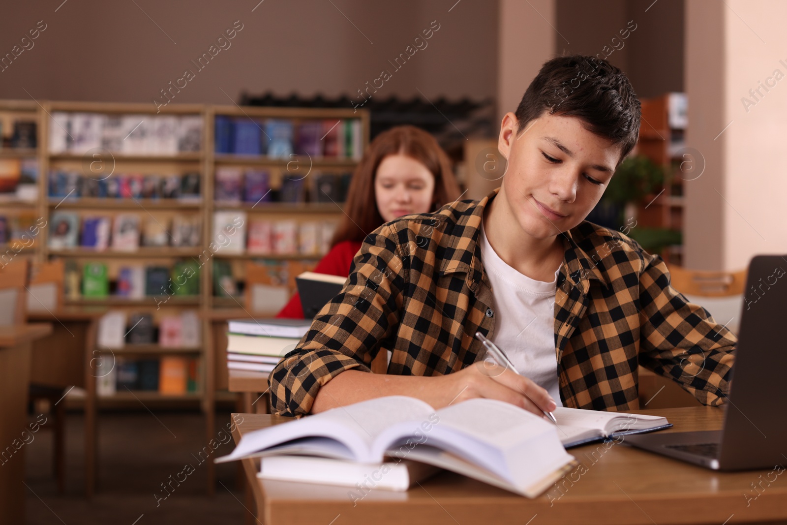 Photo of Boy taking notes at desk in public library, space for text