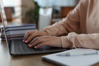 Photo of Girl using laptop at wooden desk in public library, closeup