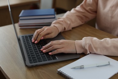 Photo of Girl using laptop at wooden desk in public library, closeup