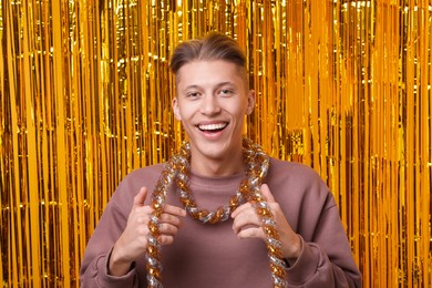 Photo of Happy young man with tinsel against golden foil curtain