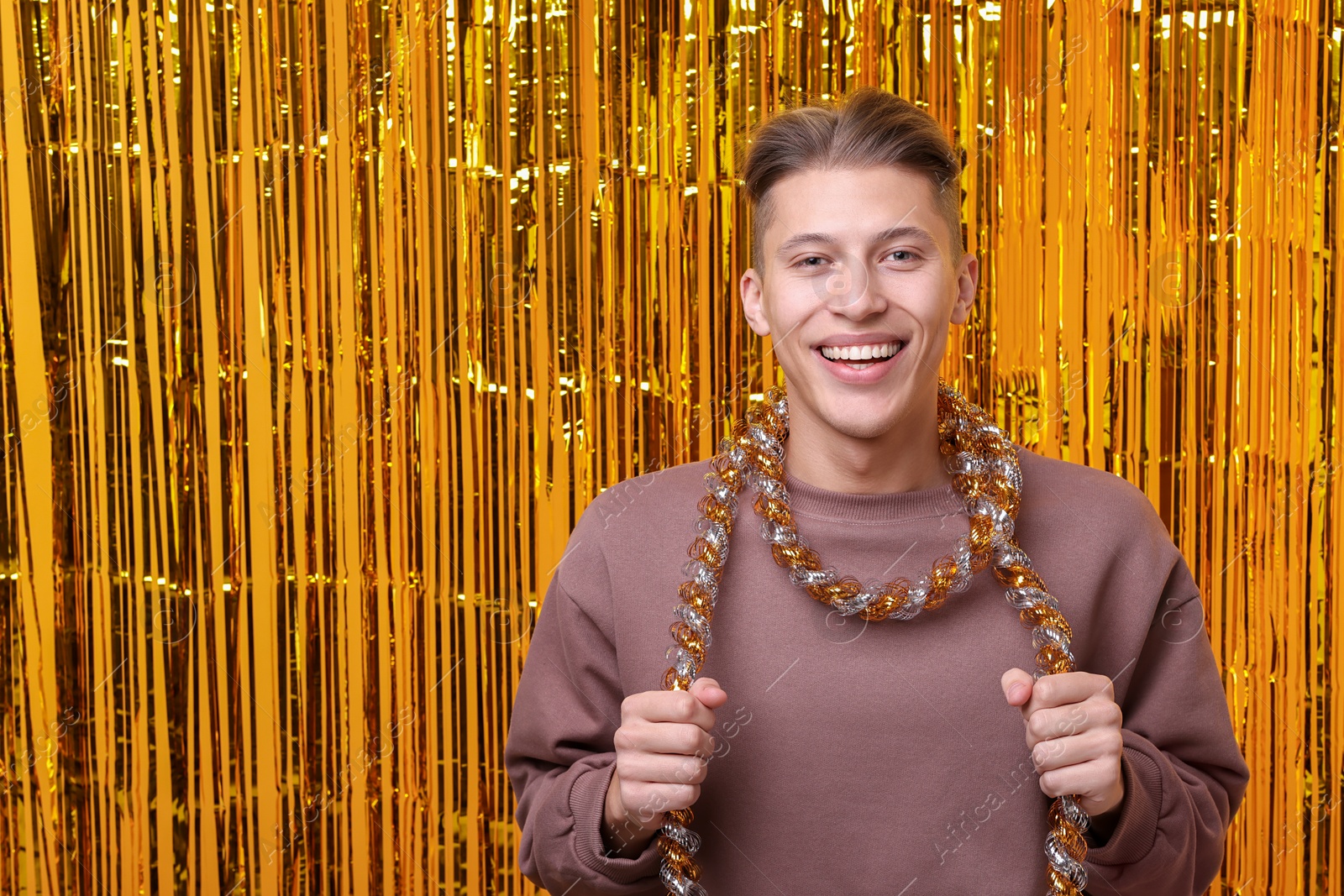 Photo of Happy young man with tinsel against golden foil curtain