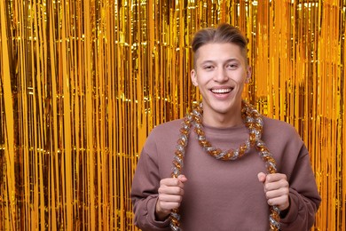 Photo of Happy young man with tinsel against golden foil curtain