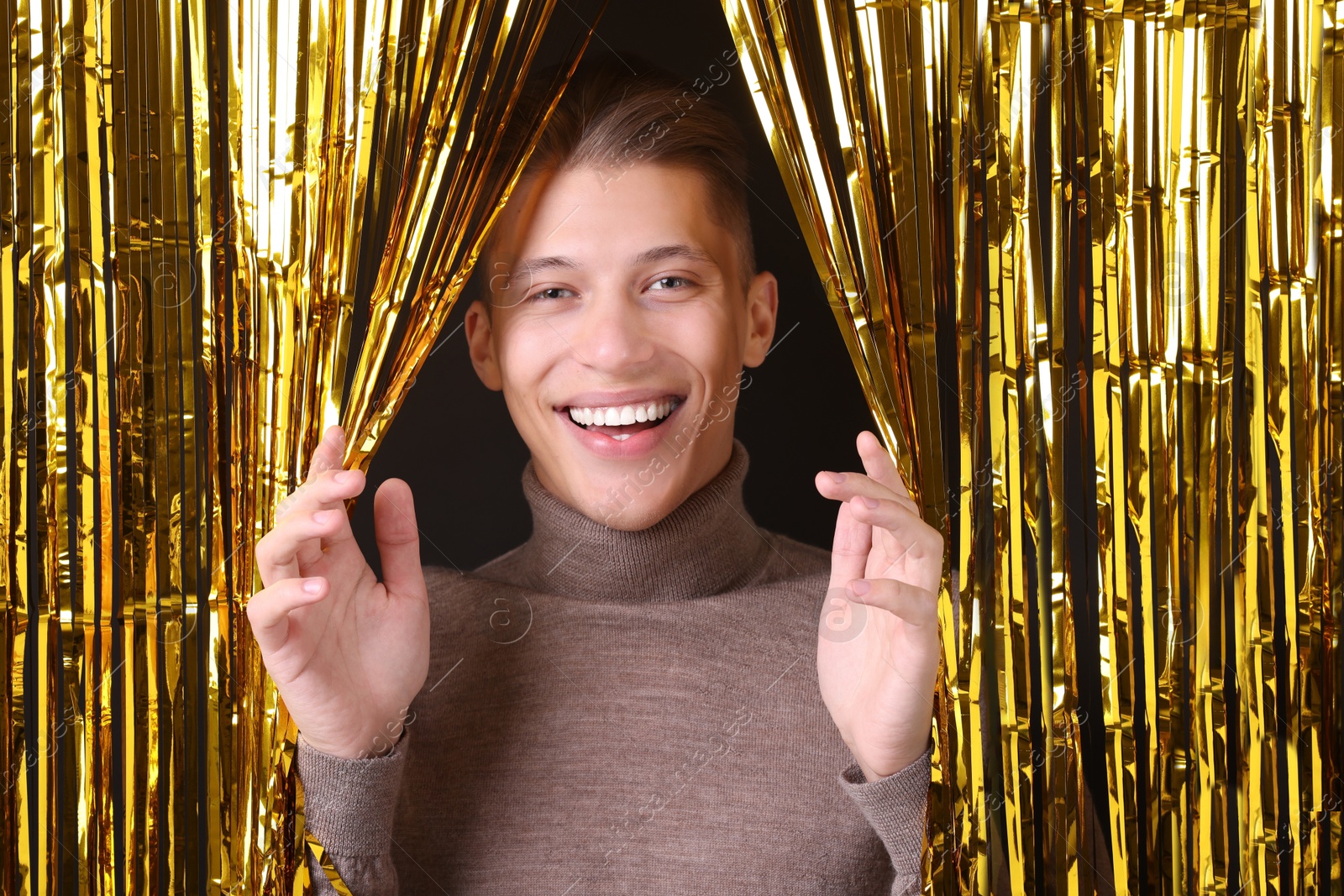 Photo of Happy young man looking out through golden foil curtain against dark background