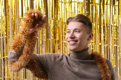 Photo of Happy young man with golden tinsel against foil curtain