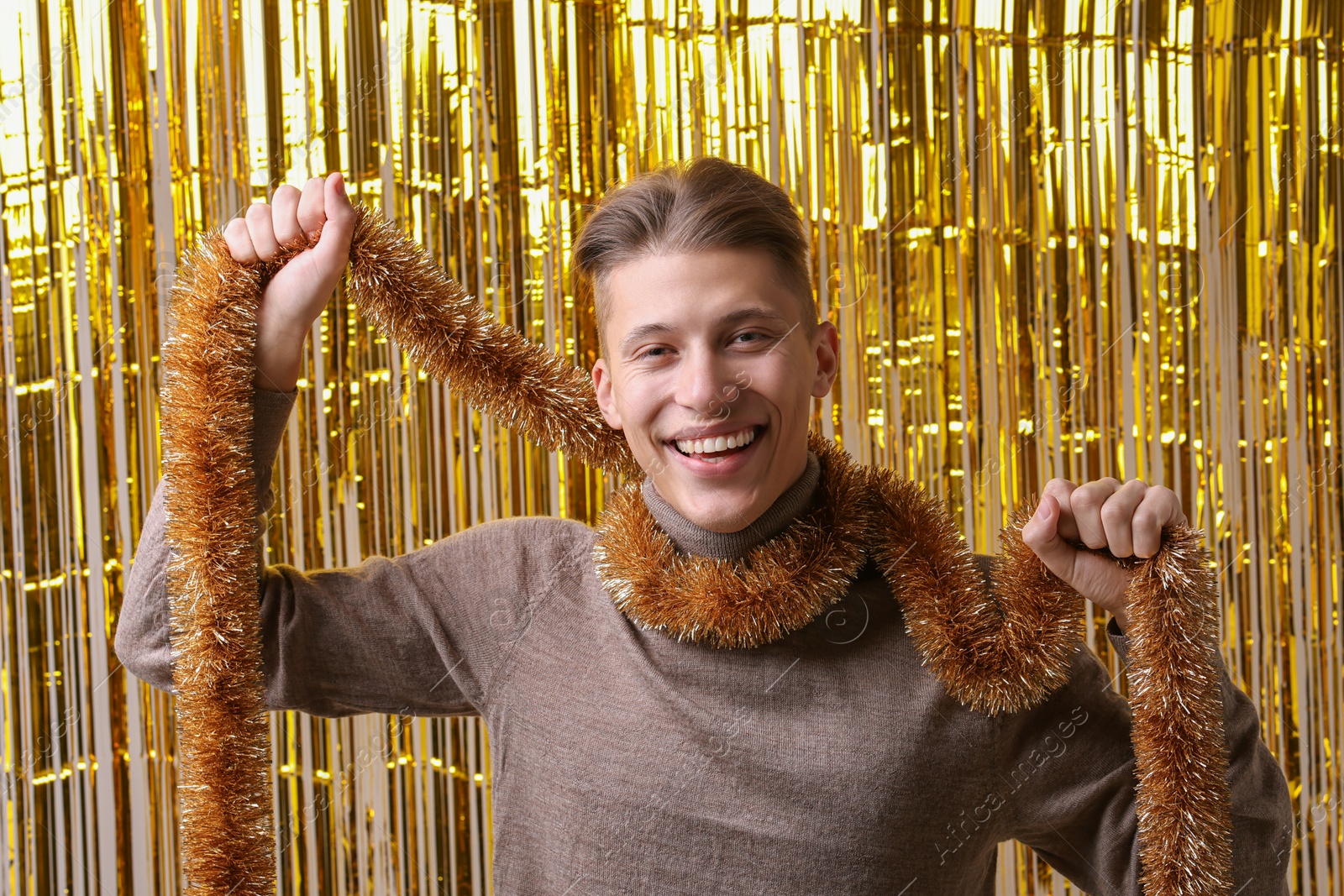 Photo of Happy young man with golden tinsel against foil curtain