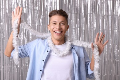 Photo of Happy young man with white tinsel against silver foil curtain