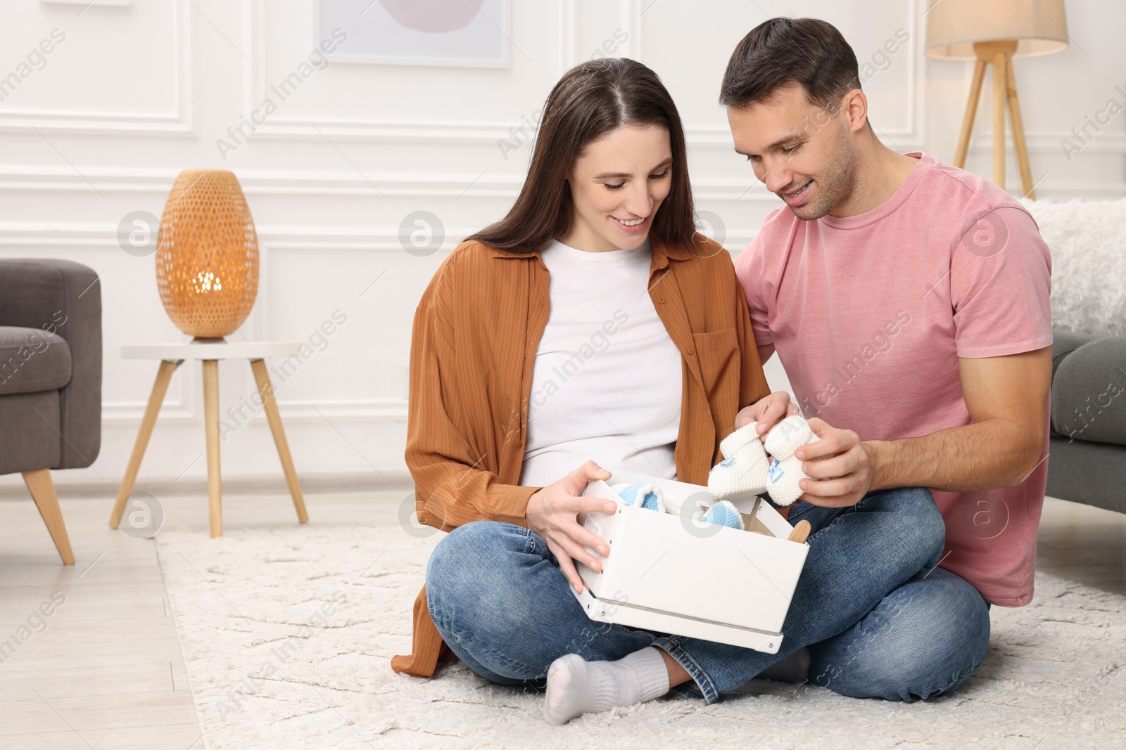 Photo of Pregnant woman and her husband with box of baby toys and booties at home. Space for text