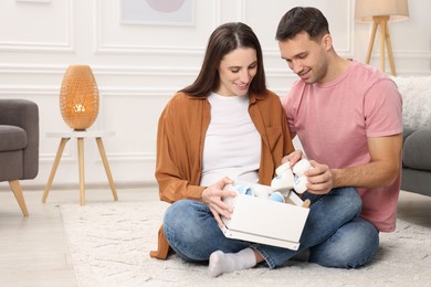 Photo of Pregnant woman and her husband with box of baby toys and booties at home. Space for text