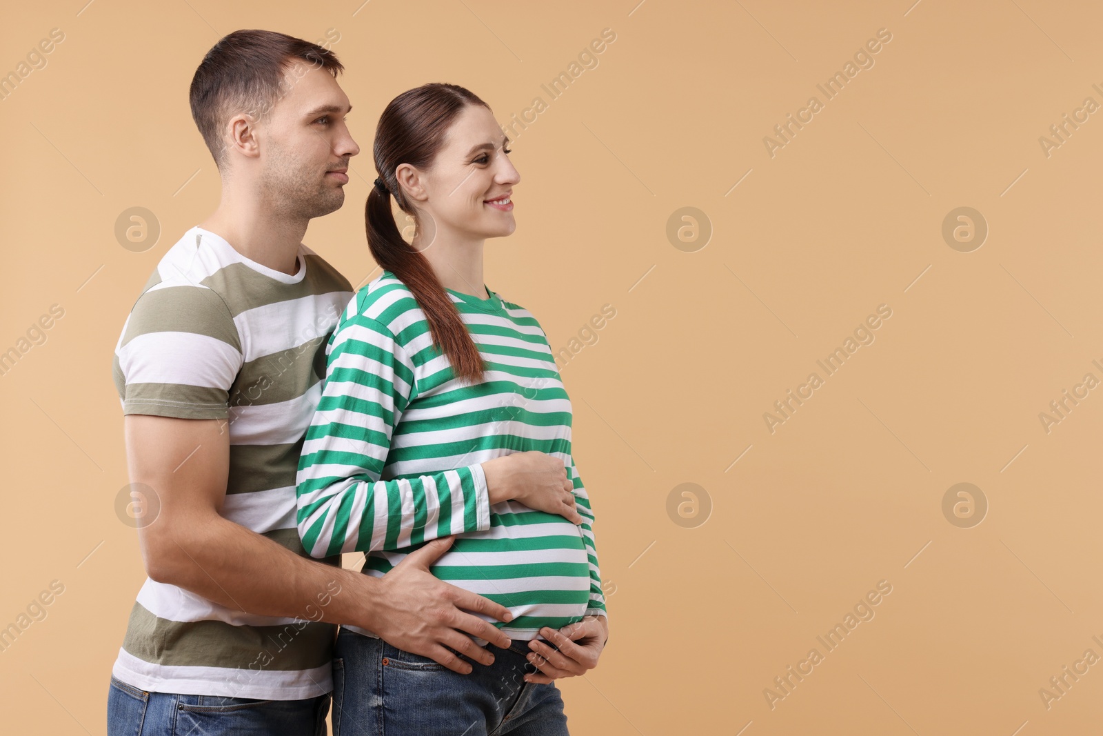 Photo of Pregnant woman and her husband on beige background. Space for text