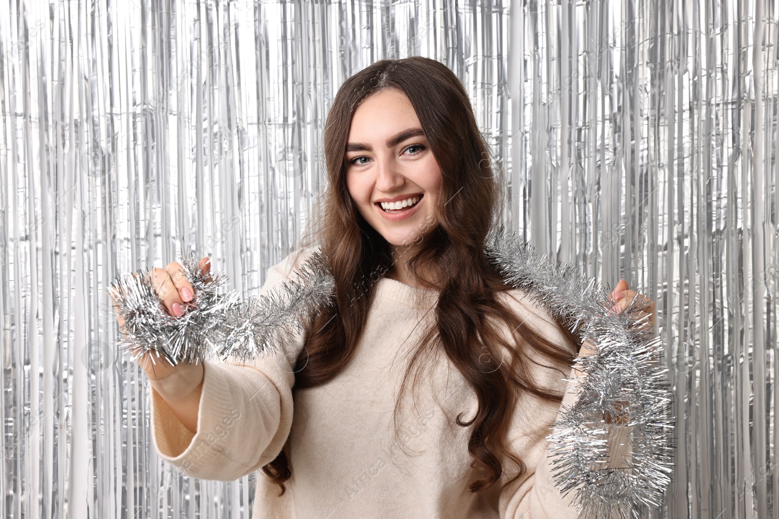 Photo of Happy young woman with tinsel against silver foil curtain