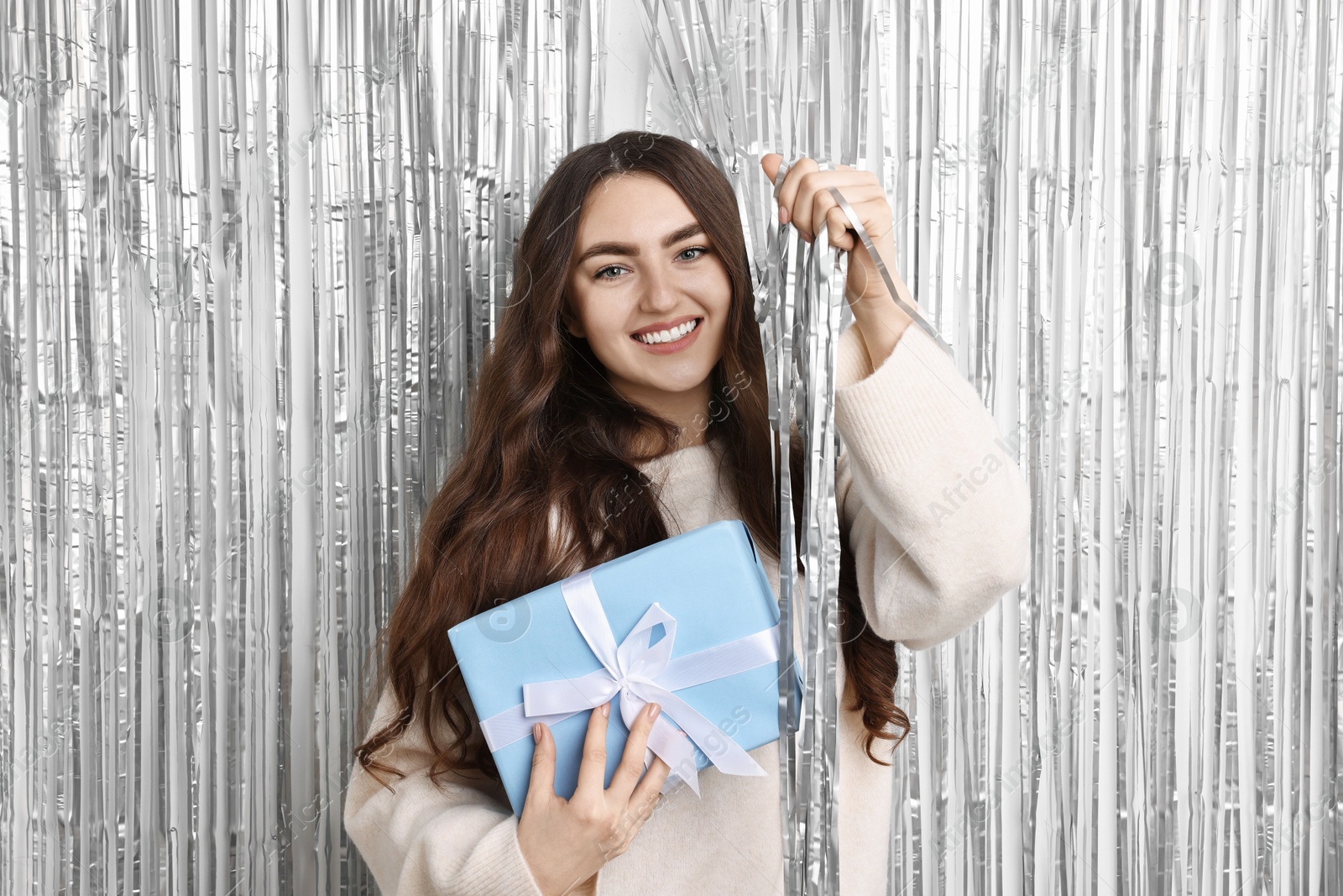 Photo of Happy young woman with gift box near silver foil curtain