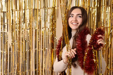 Photo of Happy young woman with tinsel near golden foil curtain against beige background. Space for text