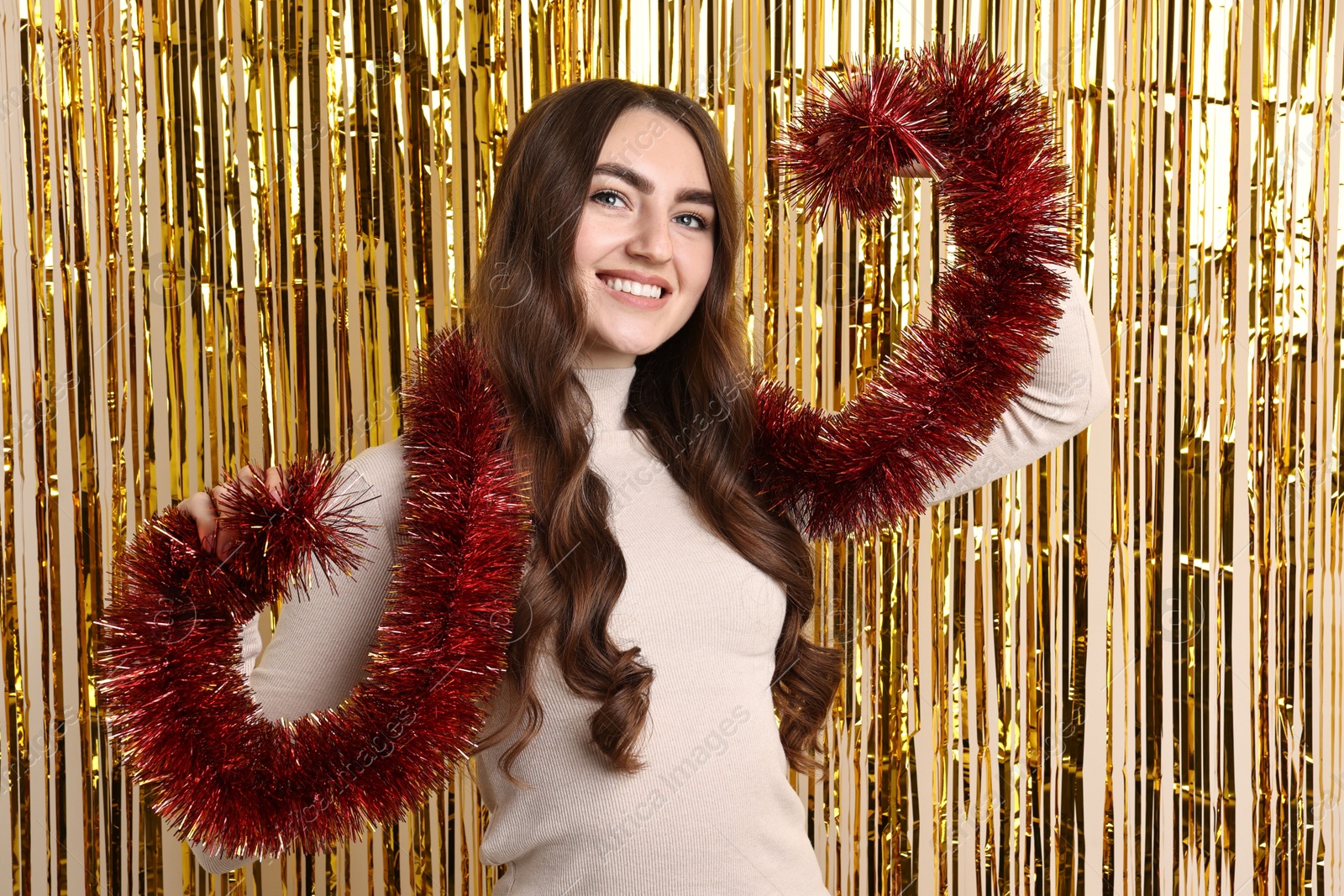 Photo of Happy young woman with tinsel against golden foil curtain