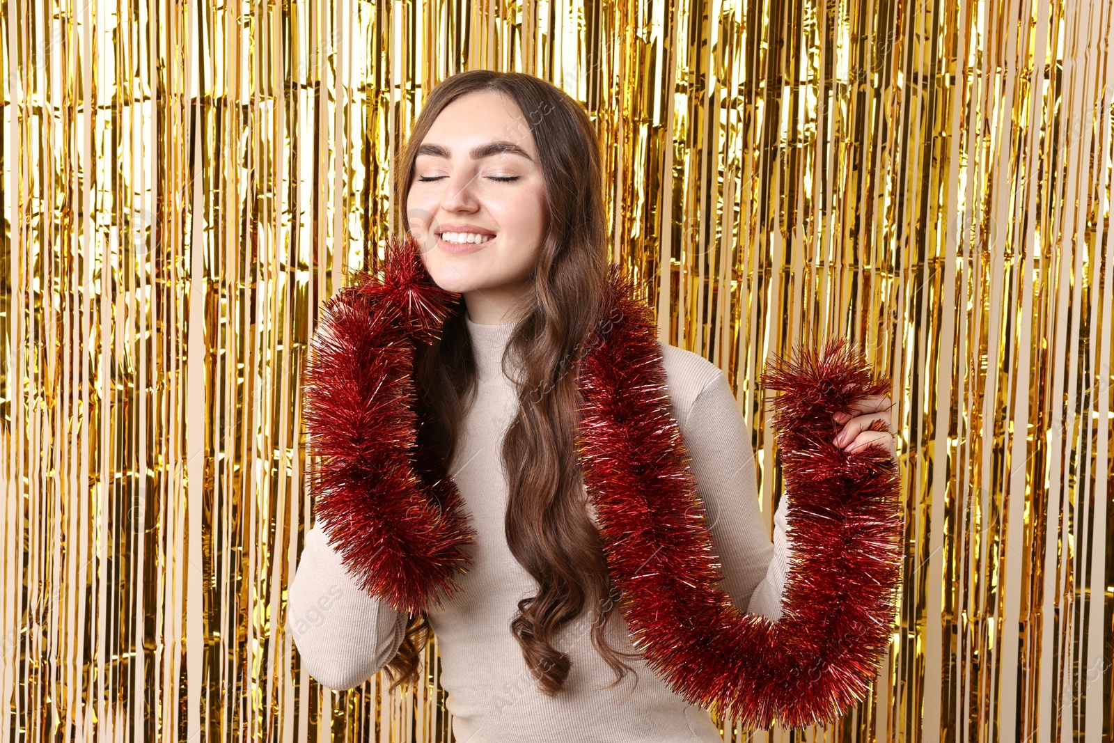 Photo of Happy young woman with tinsel against golden foil curtain