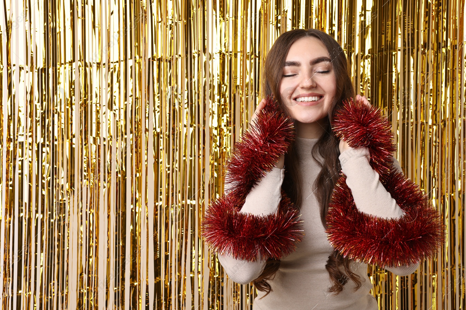 Photo of Happy young woman with tinsel against golden foil curtain. Space for text