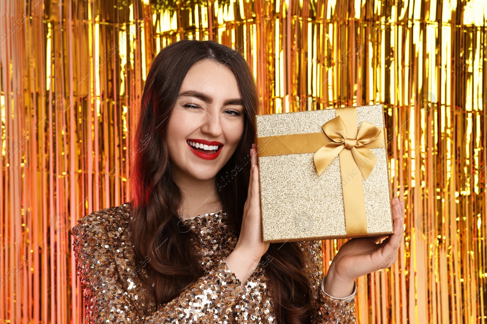 Photo of Happy young woman with gift box against golden foil curtain