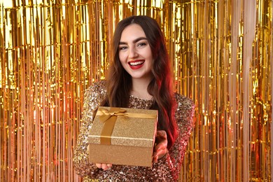 Photo of Happy young woman with gift box against golden foil curtain