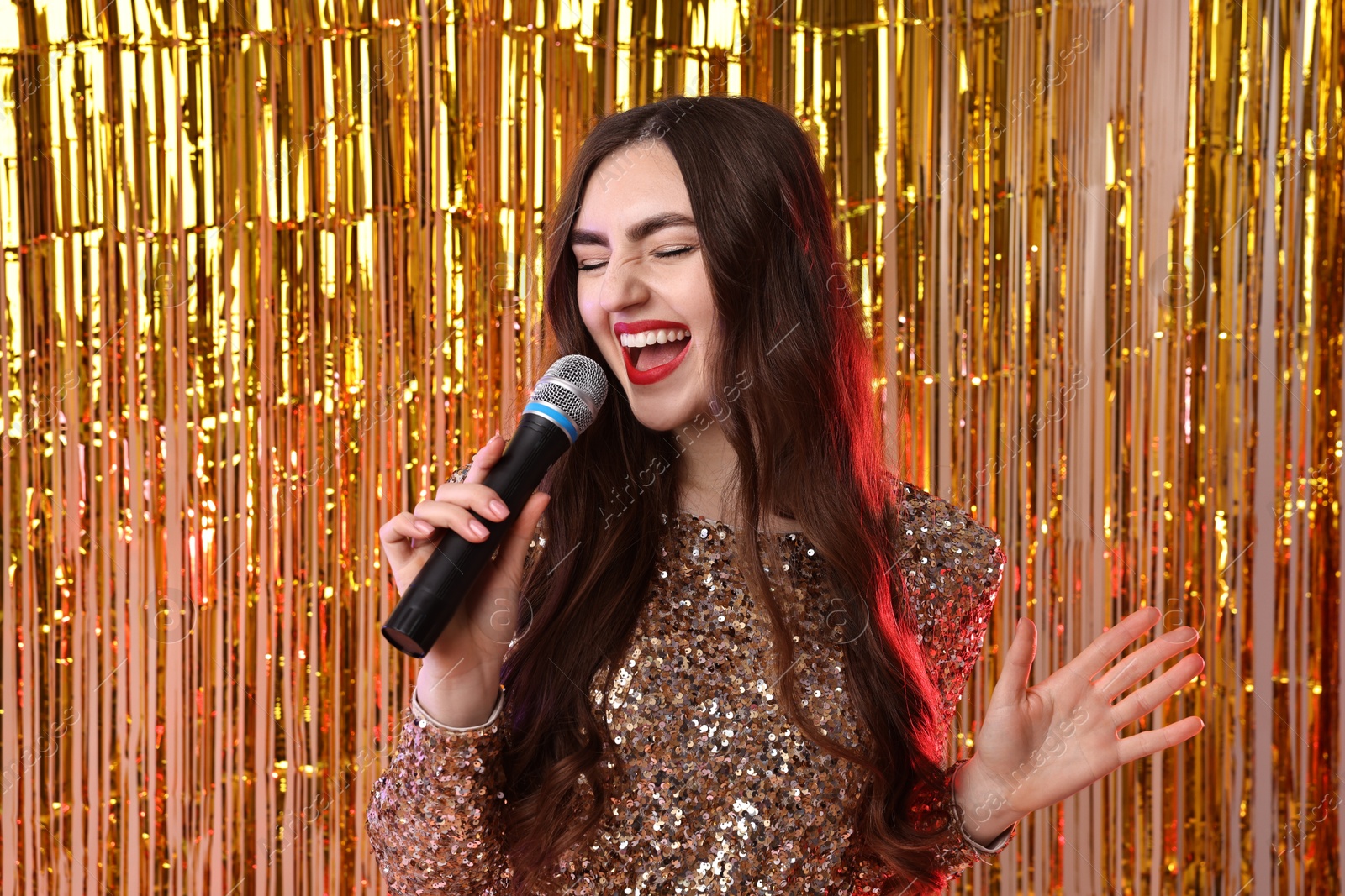 Photo of Young woman with microphone singing against foil curtain