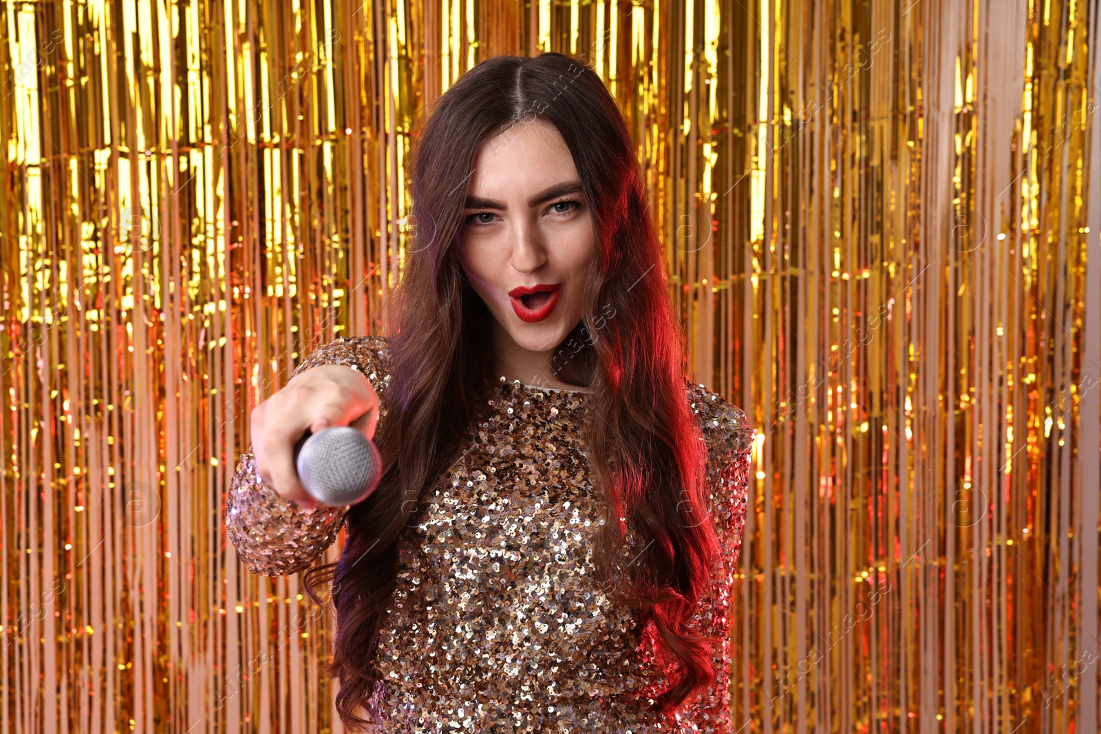 Photo of Emotional young woman with microphone against golden foil curtain