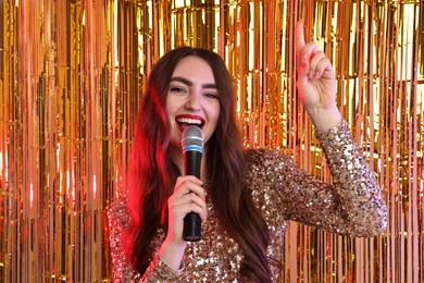 Photo of Young woman with microphone singing against foil curtain