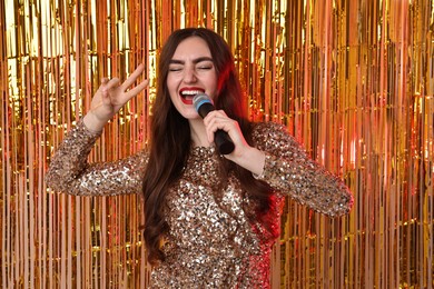 Photo of Young woman with microphone singing against foil curtain