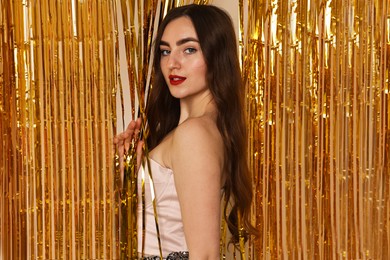 Photo of Portrait of beautiful young woman near golden foil curtain against beige background