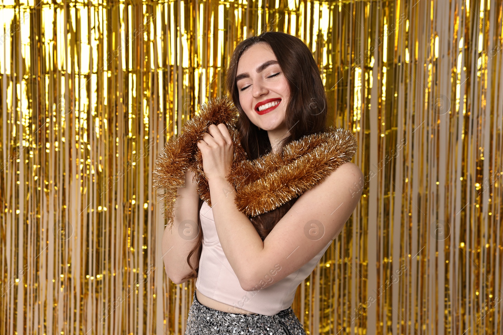 Photo of Happy young woman with tinsel against golden foil curtain