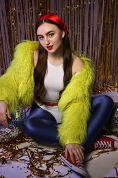 Photo of Beautiful young woman in retro outfit with shiny tinsel and disco balls indoors