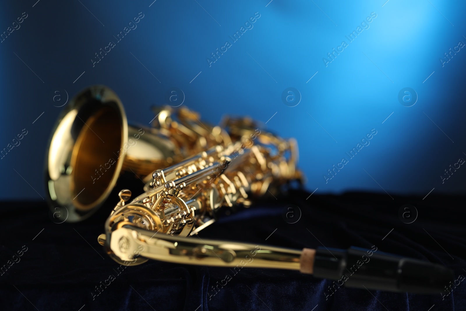 Photo of Jazz. One beautiful saxophone on dark fabric against light blue background, closeup. Space for text