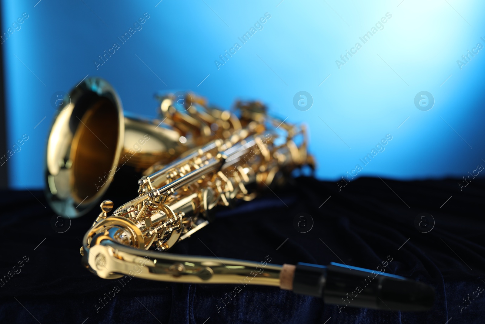 Photo of Jazz. One beautiful saxophone on dark fabric against light blue background, closeup. Space for text