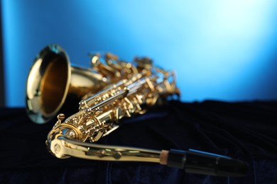 Photo of Jazz. One beautiful saxophone on dark fabric against light blue background, closeup. Space for text