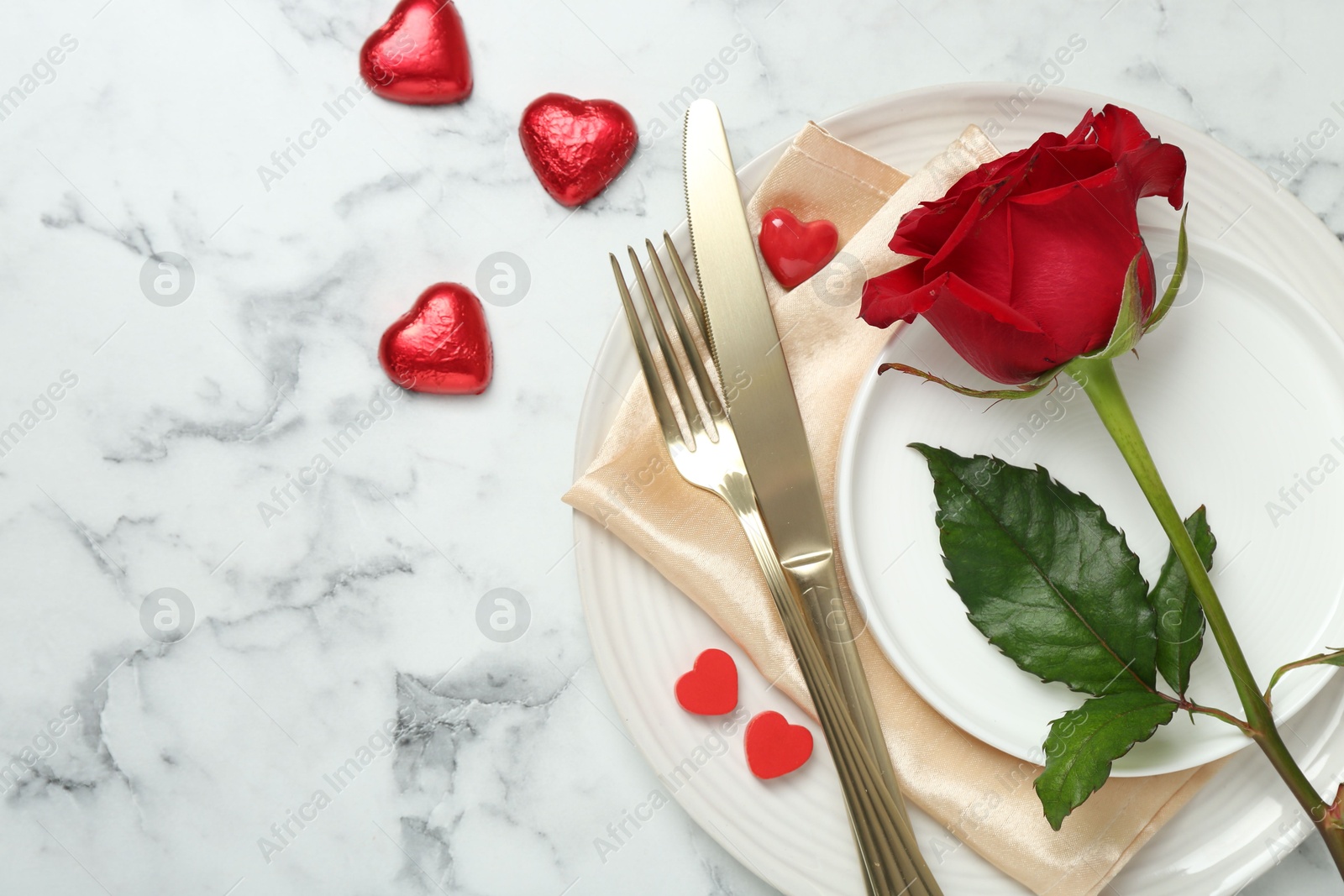 Photo of Romantic place setting for Valentine's day. Tableware, cutlery, rose and decorative hearts on white marble table, flat lay. Space for text