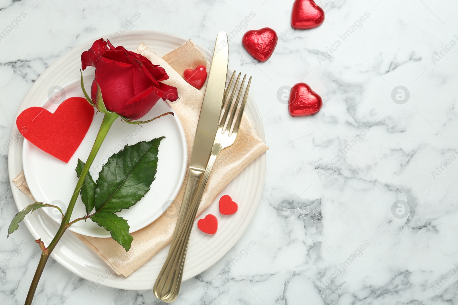 Photo of Romantic place setting for Valentine's day. Tableware, cutlery, rose and decorative hearts on white marble table, flat lay. Space for text