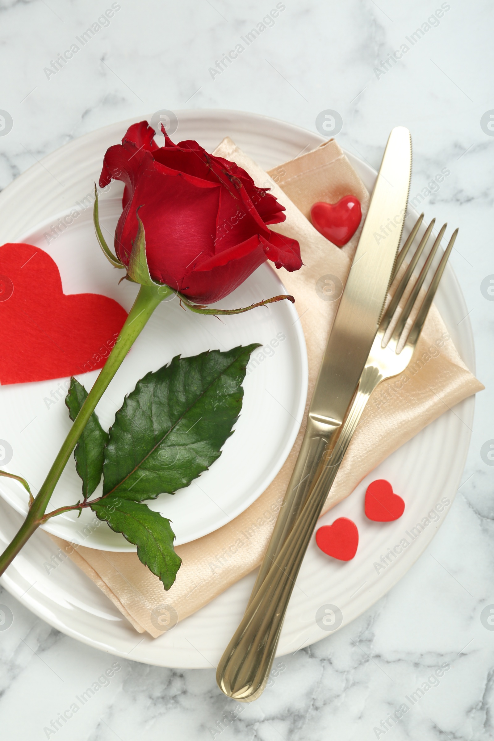 Photo of Romantic place setting for Valentine's day. Tableware, cutlery, rose and decorative hearts on white marble table, top view