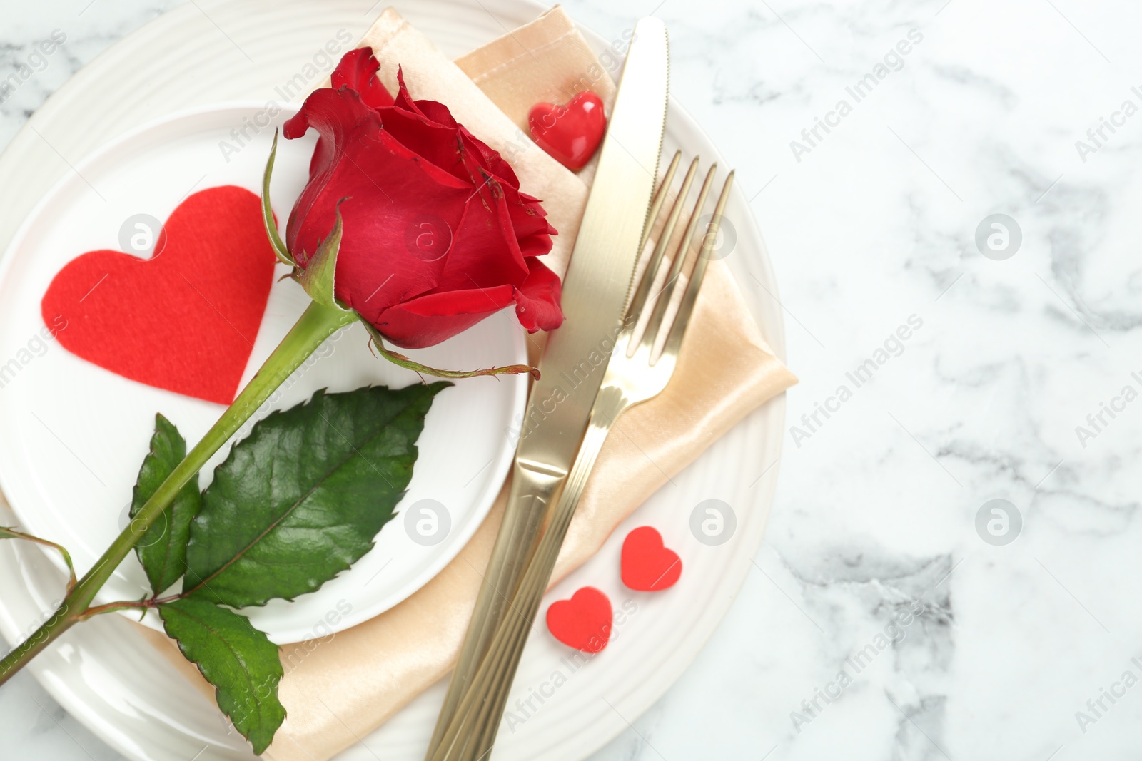 Photo of Romantic place setting for Valentine's day. Tableware, cutlery, rose and decorative hearts on white marble table, top view. Space for text