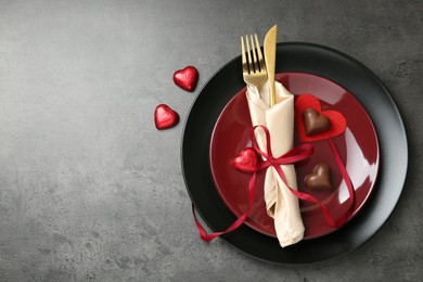 Photo of Romantic place setting for Valentine's day. Tableware, cutlery and candies in shape of hearts on grey textured table, flat lay. Space for text