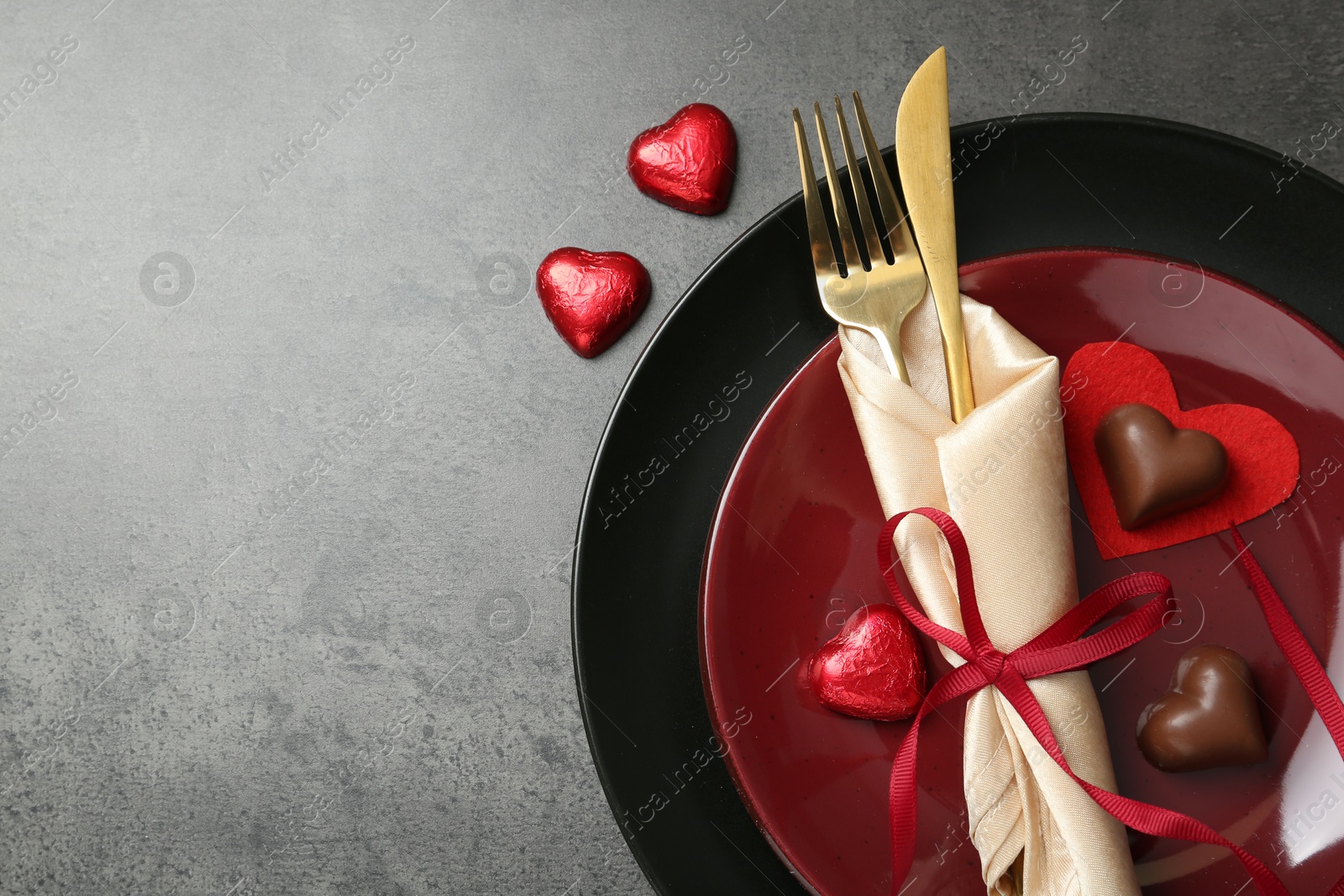 Photo of Romantic place setting for Valentine's day. Tableware, cutlery and candies in shape of hearts on grey textured table, flat lay. Space for text