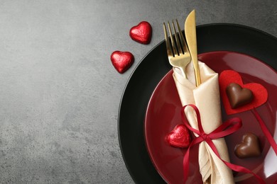 Photo of Romantic place setting for Valentine's day. Tableware, cutlery and candies in shape of hearts on grey textured table, flat lay. Space for text