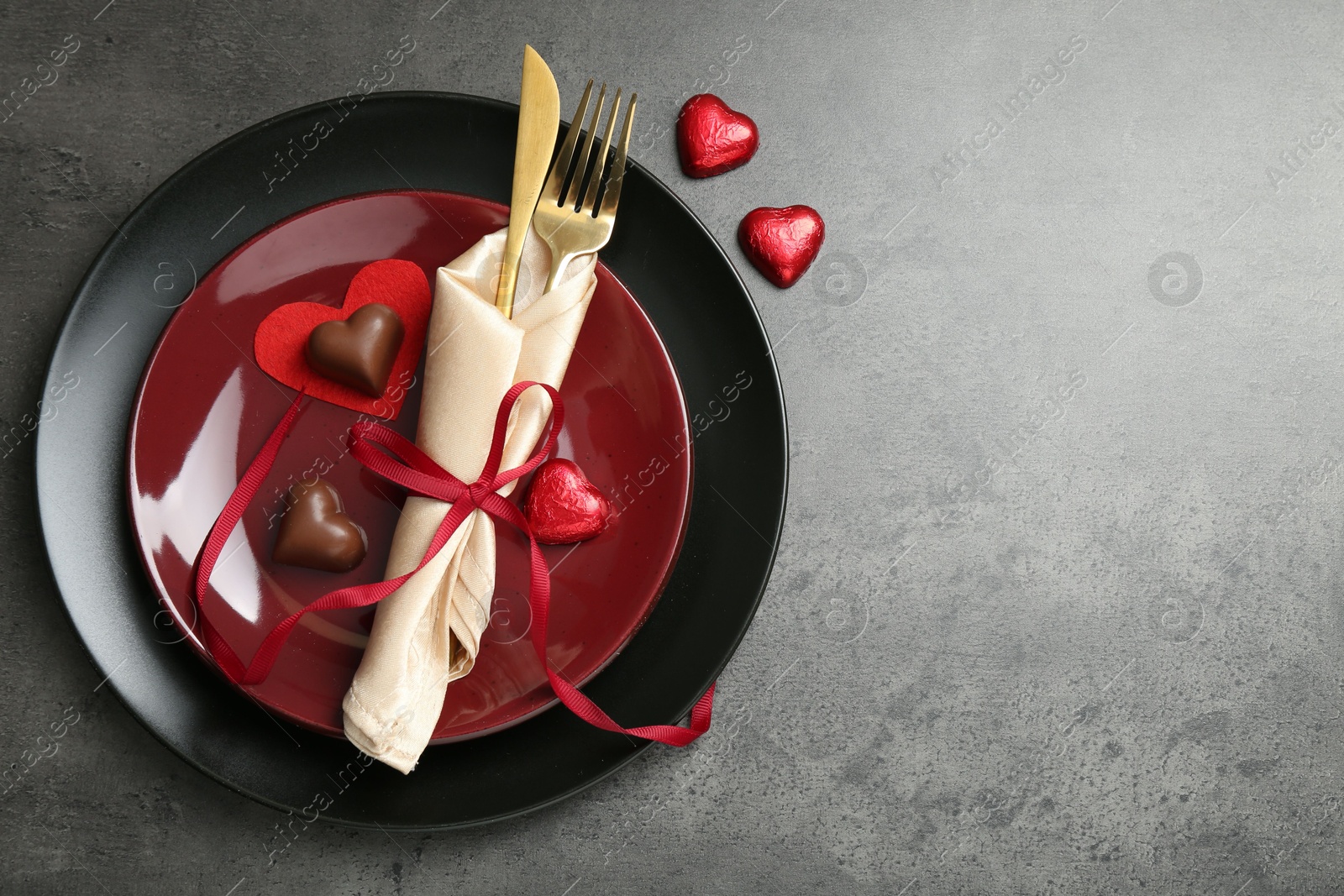 Photo of Romantic place setting for Valentine's day. Tableware, cutlery and candies in shape of hearts on grey textured table, flat lay. Space for text