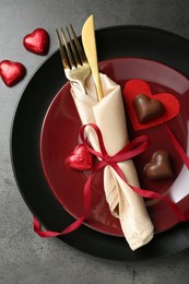 Photo of Romantic place setting for Valentine's day. Tableware, cutlery and candies in shape of hearts on grey textured table, flat lay