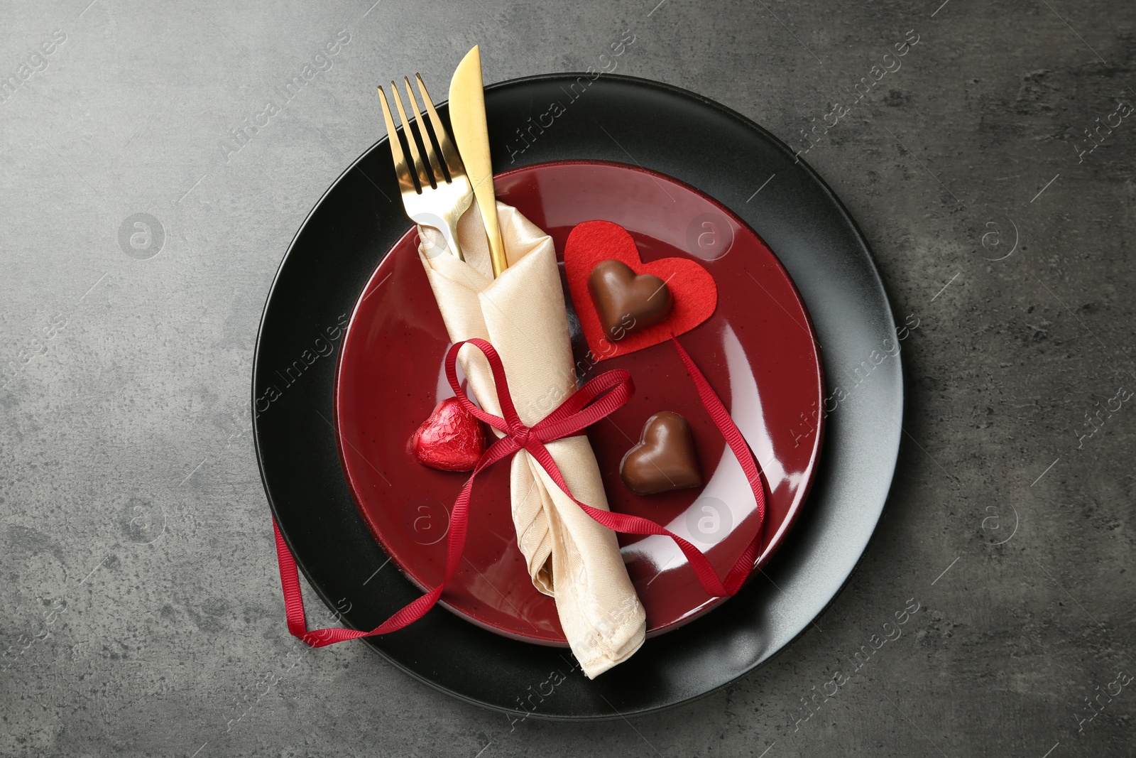 Photo of Romantic place setting for Valentine's day. Tableware, cutlery and candies in shape of hearts on grey textured table, top view